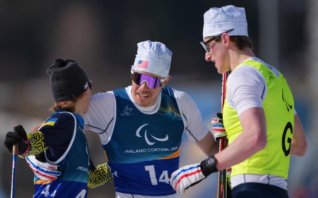 (260314) -- TESERO, March 14, 2026 (Xinhua) -- Jake Adicoff (C) of the United States communicates with Liudmyla Liashenko (L) of Ukraine after the para cross-country skiing mixed 4x2.5km relay at the Milan-Cortina 2026 Paralympic Winter Games in Tesero, Italy, March 14, 2026. (Xinhua/Lian Zhen)