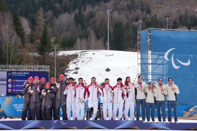 (260314) -- TESERO, March 14, 2026 (Xinhua) -- Gold medalists team China (C), silver medalists team Germany (L) and bronze medalists team Norway pose for photos during the awarding ceremony of the para cross-country skiing open 4x2.5km relay at the Milan-Cortina 2026 Paralympic Winter Games in Tesero, Italy, March 14, 2026. (Xinhua/Lian Zhen)