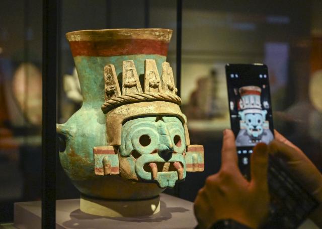 (260708) -- SHANGHAI, July 8, 2026 (Xinhua) -- A visitor takes photos of an exhibit during the exhibition "On Top of the World Tree: Ancient Civilizations of the Americas" in Shanghai, east China, July 8, 2026. The exhibition showcases a total of 1,129 sets of precious artifacts from cultural institutions in Mexico, Peru and China. It will officially open to the public on July 9 and will run until Nov. 14, 2027. (Xinhua/Chen Haoming)