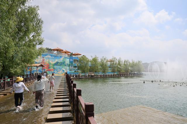 (260709) -- TIANJIN, July 9, 2026 (Xinhua) -- People enjoy their leisure time at a lake in Xiaying Town of Jizhou District, north China's Tianjin, July 8, 2026. Xiaying Town in Jizhou District of Tianjin ushered in a travel boom as the summer vacation season began in China. In recent years, the town, taking advantages of its unique mountain, forest and water resources, has built a number of distinctive tourist attractions to meet people's various travelling demands. (Xinhua/Li Ran)