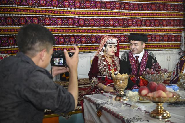 (260709) -- TAXKORGAN, July 9, 2026 (Xinhua) -- Nurkerim and his bride pose for photos at home in Taxkorgan Tajik Autonomous County, northwest China's Xinjiang Uygur Autonomous Region, June 30, 2026. The room, built by Duri Jarman in 2025, is an extension of the family's relocation house. This summer, happiness filled the air around the home of herdsman Duri Jarman. His youngest son Nurkerim tied the knot with his beloved woman. Weddings of the Tajik ethnic group usually last three days. Inscribed on the national intangible cultural heritage list in 2008, the wedding customs of the Tajik ethnic group maintain unique traditions and are always described as festivals of music, dance and food to showcase the resplendent newlyweds and their propitious marriage.
  In Aimin Village, this wedding also serves as a vivid epitome of the eight-year transformative leap brought by the poverty alleviation relocation program.
  In the winter of 2018, Jarman and his family benefited from the relocation policy for poverty alleviation and settled in Aimin Village. They gradually adapted to the changes, enjoying a new life different from that of their ancestors. Jarman ran a small grocery store with Nurkerim, while his eldest and second sons both landed stable new jobs. Nurkerim also bought a pickup truck to run a transport business. It was this business that brought him together with his wife. For this family, the relocation is not only an opportunity for development, but also a path leading to happiness.
  Over the past eight years, Jarman has expanded his courtyard and planted saplings year after year. His small yard, where not a single tree used to grow, is now shaded by lush, thriving woods. As relocation sites of the poverty alleviation relocation program, Aimin Village and neighboring Fumin Village are now home to 321 households, with at least one person employed per household on average. (Xinhua/Hu Huhu)
