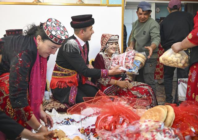 (260709) -- TAXKORGAN, July 9, 2026 (Xinhua) -- Relatives and friends lay out wedding gifts in front of the newlyweds in Taxkorgan Tajik Autonomous County, northwest China's Xinjiang Uygur Autonomous Region, June 30, 2026. This summer, happiness filled the air around the home of herdsman Duri Jarman. His youngest son Nurkerim tied the knot with his beloved woman. Weddings of the Tajik ethnic group usually last three days. Inscribed on the national intangible cultural heritage list in 2008, the wedding customs of the Tajik ethnic group maintain unique traditions and are always described as festivals of music, dance and food to showcase the resplendent newlyweds and their propitious marriage.
  In Aimin Village, this wedding also serves as a vivid epitome of the eight-year transformative leap brought by the poverty alleviation relocation program.
  In the winter of 2018, Jarman and his family benefited from the relocation policy for poverty alleviation and settled in Aimin Village. They gradually adapted to the changes, enjoying a new life different from that of their ancestors. Jarman ran a small grocery store with Nurkerim, while his eldest and second sons both landed stable new jobs. Nurkerim also bought a pickup truck to run a transport business. It was this business that brought him together with his wife. For this family, the relocation is not only an opportunity for development, but also a path leading to happiness.
  Over the past eight years, Jarman has expanded his courtyard and planted saplings year after year. His small yard, where not a single tree used to grow, is now shaded by lush, thriving woods. As relocation sites of the poverty alleviation relocation program, Aimin Village and neighboring Fumin Village are now home to 321 households, with at least one person employed per household on average. (Xinhua/Hu Huhu)