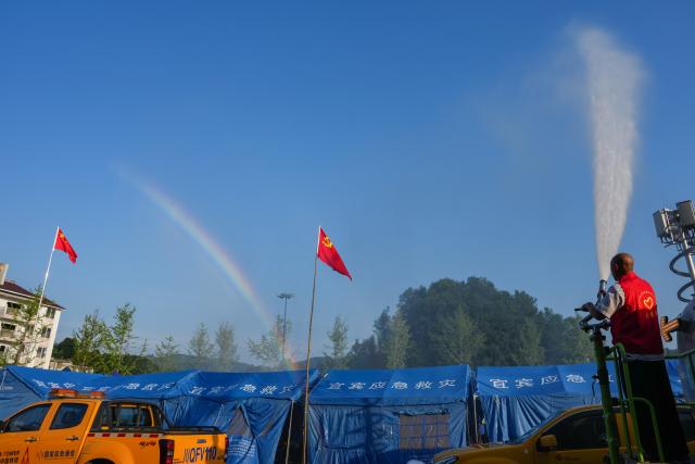 (260709) -- YIBIN, July 9, 2026 (Xinhua) -- A volunteer sprays water for cooling a temporary resettlement site for quake-affected people in Qunle Village of Gaoxian County, Yibin City, southwest China's Sichuan Province, July 9, 2026. A 5.0-magnitude earthquake jolted Gaoxian County, Yibin City, at 10:08 a.m. on Wednesday (Beijing Time), according to the China Earthquake Networks Center (CENC). Local authorities are making sustained efforts to ensure sound resettlement of quake-affected people. (Xinhua/Wang Xi)