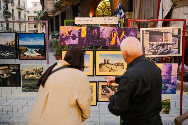 (260709) -- CAIRO, July 9, 2026 (Xinhua) -- Tourists view paintings in downtown Cairo, Egypt, July 9, 2026. Egypt's government recently launched the "Street of Art" initiative, aiming to transform the streets and squares of the capital, Cairo, into open-air cultural spaces. Every Thursday through Saturday evening, the public can enjoy free cultural activities such as poetry readings, musical performances, and visual art exhibitions, attracting active participation from both citizens and tourists. (Xinhua/Xin Mengchen)