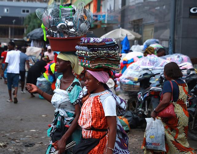 (260710) -- ABIDJAN, July 10, 2026 (Xinhua) -- Women carry daily necessities and local fabrics for sale along the street in Abidjan, Cote d'Ivoire, on July 9, 2026. (Photo by Yvan Sonh/Xinhua)