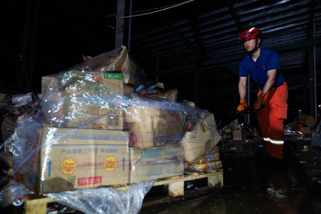 (260710) -- HUANGGANG, July 10, 2026 (Xinhua) -- A rescuer transfers supplies at a tornado-affected logistics park in Huangzhou District of Huanggang, central China's Hubei Province, July 9, 2026. A large batch of essential supplies including rice, flour, grains, edible oil, and convenience foods had been put at risk of water damage inside a logistics park of Huanggang since a tornado hit the city on Monday. Rescuers worked around the clock and successfully relocated the supplies to designated storage sites after more than 10 hours of effort from Thursday afternoon to Friday morning. (Xinhua/Wu Zhizun)