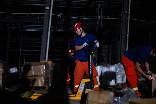 (260710) -- HUANGGANG, July 10, 2026 (Xinhua) -- Rescuers transfer supplies at a tornado-affected logistics park in Huangzhou District of Huanggang, central China's Hubei Province, July 9, 2026. A large batch of essential supplies including rice, flour, grains, edible oil, and convenience foods had been put at risk of water damage inside a logistics park of Huanggang since a tornado hit the city on Monday. Rescuers worked around the clock and successfully relocated the supplies to designated storage sites after more than 10 hours of effort from Thursday afternoon to Friday morning. (Xinhua/Wu Zhizun)