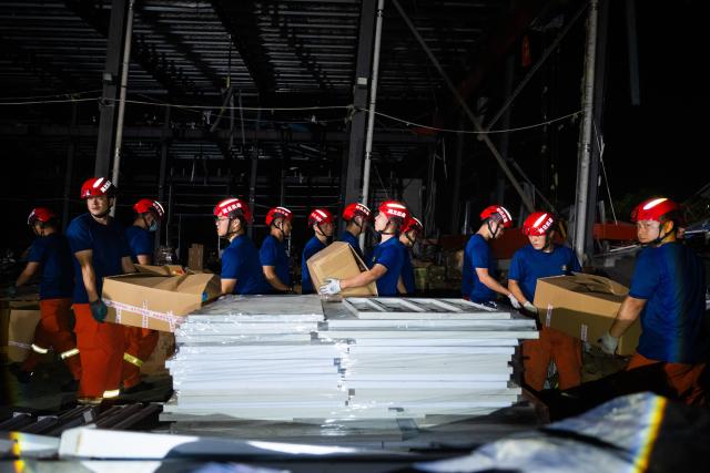 (260710) -- HUANGGANG, July 10, 2026 (Xinhua) -- Rescuers transfer supplies at a tornado-affected logistics park in Huangzhou District of Huanggang, central China's Hubei Province, July 9, 2026. A large batch of essential supplies including rice, flour, grains, edible oil, and convenience foods had been put at risk of water damage inside a logistics park of Huanggang since a tornado hit the city on Monday. Rescuers worked around the clock and successfully relocated the supplies to designated storage sites after more than 10 hours of effort from Thursday afternoon to Friday morning. (Xinhua/Wu Zhizun)