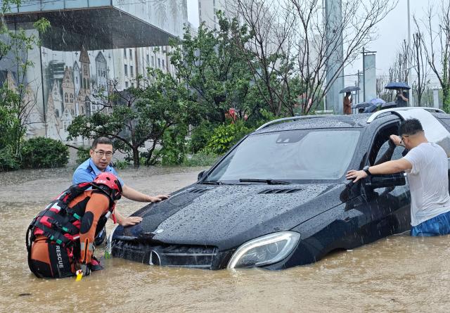 (260713) -- SHENYANG, July 13, 2026 (Xinhua) -- A police officer and firefighter help rescue a stranded car amid rain in Shenyang, northeast China's Liaoning Province, on July 13, 2026. From Sunday to Monday, heavy to torrential rain lashed central Liaoning Province. Several cities, including Shenyang and Fushun, suspended classes, business operations and work on Monday as a precaution, while water levels in several rivers rose significantly due to the heavy rainfall. (Xinhua/Li Gang)