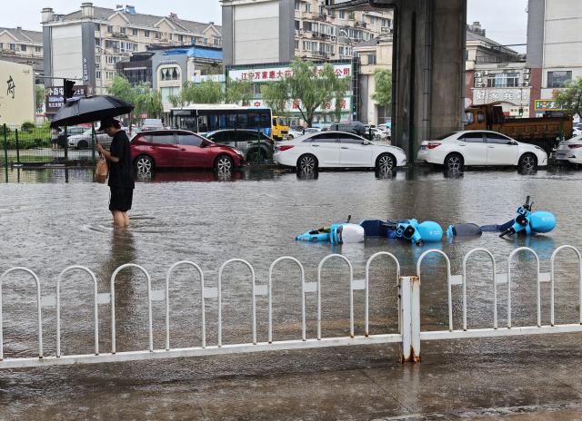 (260713) -- SHENYANG, July 13, 2026 (Xinhua) -- A man walks on a flooded road amid rain in Shenyang, northeast China's Liaoning Province, on July 13, 2026. From Sunday to Monday, heavy to torrential rain lashed central Liaoning Province. Several cities, including Shenyang and Fushun, suspended classes, business operations and work on Monday as a precaution, while water levels in several rivers rose significantly due to the heavy rainfall. (Xinhua/Li Gang)