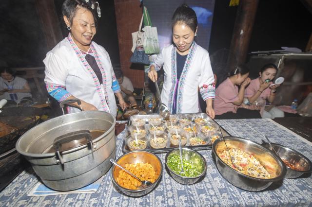 (260713) -- CONGJIANG, July 13, 2026 (Xinhua) -- People of the Dong ethnic make local specialty foods during a musical event in Congjiang County of southwest China's Guizhou Province, July 12, 2026. The event featuring performing arts of the Dong ethnic group and local specialty foods was held here on Sunday, attracting hundreds of tourists. (Photo by Wu Dejun/Xinhua)