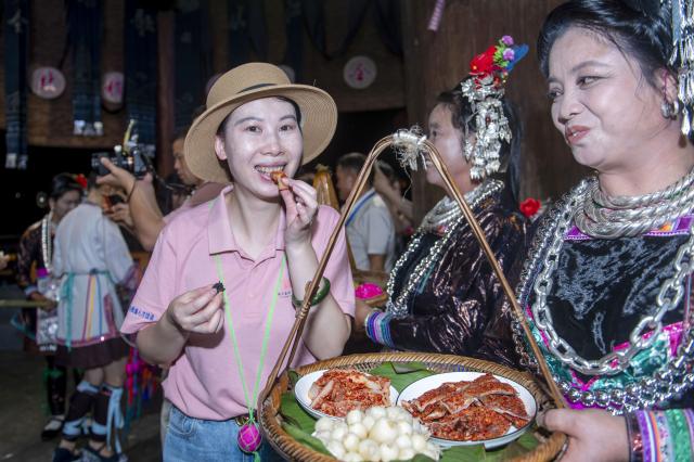 (260713) -- CONGJIANG, July 13, 2026 (Xinhua) -- A tourist tries local specialty foods during a musical event in Congjiang County of southwest China's Guizhou Province, July 12, 2026. The event featuring performing arts of the Dong ethnic group and local specialty foods was held here on Sunday, attracting hundreds of tourists. (Photo by Wu Dejun/Xinhua)
