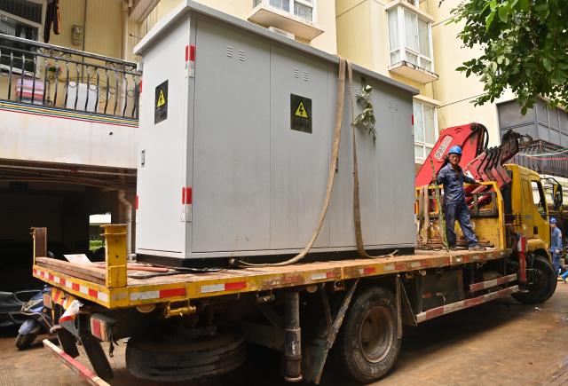 (260714) -- GUIGANG, July 14, 2026 (Xinhua) -- Staff members bring power device for replacement into a residential compound in Guigang City, south China's Guangxi Zhuang Autonomous Region, July 14, 2026. The power supplier in Guigang has mobilized all hands available to restore power supply as flooding inflicted by typhoon Maysak subsides in the city. (Xinhua/Lu Boan)