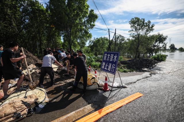 (260714) -- SHENYANG, July 14, 2026 (Xinhua) -- Emergency workers fill sandbags at a dike at Yujiatai Village of Liaozhong District, Shenyang, northeast China's Liaoning Province, July 14, 2026. Emergency responding workers in riverside towns and villages of Liaozhong District of Shenyang are working to heighten and fortify the dikes as upstream flood discharge continues to rise the water level in the river. (Xinhua/Pan Yulong)