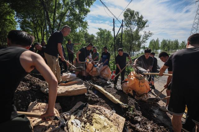 (260714) -- SHENYANG, July 14, 2026 (Xinhua) -- Emergency workers fill sandbags at a dike at Yujiatai Village of Liaozhong District, Shenyang, northeast China's Liaoning Province, July 14, 2026. Emergency responding workers in riverside towns and villages of Liaozhong District of Shenyang are working to heighten and fortify the dikes as upstream flood discharge continues to rise the water level in the river. (Xinhua/Pan Yulong)