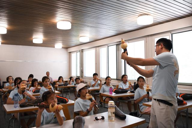 (260715) -- BERN, July 15, 2026 (Xinhua) -- Members of a Chinese culture summer camp learn about Hulusi, a traditional Chinese wind instrument, in Bern, Switzerland, July 14, 2026. A summer camp featuring traditional Chinese culture opened here on Tuesday. (Xinhua/Lian Yi)