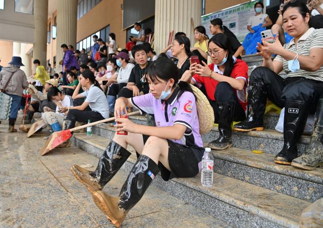 (260715) -- NANNING, July 15, 2026 (Xinhua) -- People take a break during the clearing work at a middle school in Guigang City, south China's Guangxi Zhuang Autonomous Region, July 15, 2026. Efforts are underway to facilitate flood relief and recovery in Guangxi, which has been hit by severe rainstorms and flooding caused by Typhoon Maysak. (Xinhua/Lu Boan)