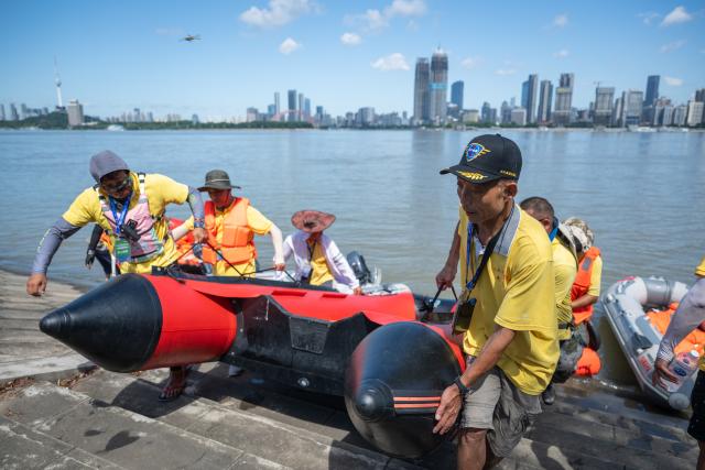 (260717) -- WUHAN, July 17, 2026 (Xinhua) -- Members of Yangtze River volunteer lifeguard team carry an inflatable boat ashore after a trial event before the 51st edition of the Yangtze River crossing event in Wuhan, central China's Hubei Province, July 9, 2026. Located at the confluence of the Yangtze River and its longest tributary, the Han River, Wuhan is home to 165 rivers and 166 lakes. These abundant water resources foster a deep-seated love for open-water swimming among Wuhan's inhabitants.
   This year marks the 51st edition of the Yangtze River crossing event. During the competition, swimmers from around the country and the world gather on the banks of the Yangtze River to race across the river. Yet behind every crossing, members of a volunteer team, the Yangtze River volunteer lifeguard team, always safeguard participants' safety with passion, courage and selfless dedication.
   Zhou Zhuan, 64, is a detachment captain of the Yangtze River volunteer lifeguard Team. This year marks his fourth time participating in rescue support work during the river crossing event. As a native of Wuhan who grew up by the river, Zhou has a deep affection for the Yangtze River. Having loved swimming for many years and wishing to contribute to the community, Zhou joined the team after retiring from work in 2017.
   On regular days, Zhou and team members conduct swimming training and riverbank patrols, carry out simulated rescues, and deliver safety awareness outreach program. During the summer flood season, members of the team take turns on duty along the riverbank to respond to emergencies. Established in 2010, the team now comprises over 3,500 members and has rescued more than 1,200 people to date. (Xinhua/Du Zixuan)