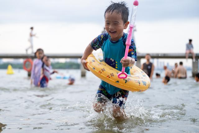(260717) -- WUHAN, July 17, 2026 (Xinhua) -- A child paly at the water area near Wuhan University in Wuhan, central China's Hubei Province, July 15, 2026. Located at the confluence of the Yangtze River and its longest tributary, the Han River, Wuhan is home to 165 rivers and 166 lakes. These abundant water resources foster a deep-seated love for open-water swimming among Wuhan's inhabitants.
   This year marks the 51st edition of the Yangtze River crossing event. During the competition, swimmers from around the country and the world gather on the banks of the Yangtze River to race across the river. Yet behind every crossing, members of a volunteer team, the Yangtze River volunteer lifeguard team, always safeguard participants' safety with passion, courage and selfless dedication.
   Zhou Zhuan, 64, is a detachment captain of the Yangtze River volunteer lifeguard Team. This year marks his fourth time participating in rescue support work during the river crossing event. As a native of Wuhan who grew up by the river, Zhou has a deep affection for the Yangtze River. Having loved swimming for many years and wishing to contribute to the community, Zhou joined the team after retiring from work in 2017.
   On regular days, Zhou and team members conduct swimming training and riverbank patrols, carry out simulated rescues, and deliver safety awareness outreach program. During the summer flood season, members of the team take turns on duty along the riverbank to respond to emergencies. Established in 2010, the team now comprises over 3,500 members and has rescued more than 1,200 people to date. (Xinhua/Du Zixuan)