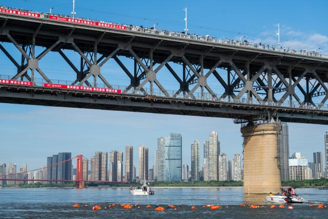 (260717) -- WUHAN, July 17, 2026 (Xinhua) -- People watch on the Yangtze River Bridge as participants compete during the 51st edition of the Yangtze River crossing event in Wuhan, central China's Hubei Province, July 16, 2026. Located at the confluence of the Yangtze River and its longest tributary, the Han River, Wuhan is home to 165 rivers and 166 lakes. These abundant water resources foster a deep-seated love for open-water swimming among Wuhan's inhabitants.
   This year marks the 51st edition of the Yangtze River crossing event. During the competition, swimmers from around the country and the world gather on the banks of the Yangtze River to race across the river. Yet behind every crossing, members of a volunteer team, the Yangtze River volunteer lifeguard team, always safeguard participants' safety with passion, courage and selfless dedication.
   Zhou Zhuan, 64, is a detachment captain of the Yangtze River volunteer lifeguard Team. This year marks his fourth time participating in rescue support work during the river crossing event. As a native of Wuhan who grew up by the river, Zhou has a deep affection for the Yangtze River. Having loved swimming for many years and wishing to contribute to the community, Zhou joined the team after retiring from work in 2017.
   On regular days, Zhou and team members conduct swimming training and riverbank patrols, carry out simulated rescues, and deliver safety awareness outreach program. During the summer flood season, members of the team take turns on duty along the riverbank to respond to emergencies. Established in 2010, the team now comprises over 3,500 members and has rescued more than 1,200 people to date. (Xinhua/Du Zixuan)