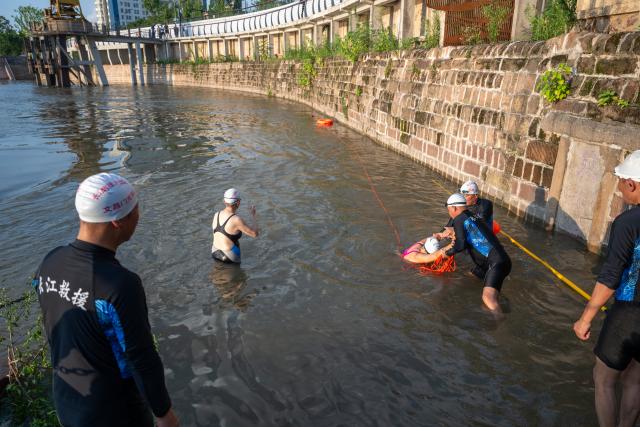 (260717) -- WUHAN, July 17, 2026 (Xinhua) -- Members of Yangtze River volunteer lifeguard team conduct a simulated water rescue at a park in Wuhan, central China's Hubei Province, July 10, 2026. Located at the confluence of the Yangtze River and its longest tributary, the Han River, Wuhan is home to 165 rivers and 166 lakes. These abundant water resources foster a deep-seated love for open-water swimming among Wuhan's inhabitants.
   This year marks the 51st edition of the Yangtze River crossing event. During the competition, swimmers from around the country and the world gather on the banks of the Yangtze River to race across the river. Yet behind every crossing, members of a volunteer team, the Yangtze River volunteer lifeguard team, always safeguard participants' safety with passion, courage and selfless dedication.
   Zhou Zhuan, 64, is a detachment captain of the Yangtze River volunteer lifeguard Team. This year marks his fourth time participating in rescue support work during the river crossing event. As a native of Wuhan who grew up by the river, Zhou has a deep affection for the Yangtze River. Having loved swimming for many years and wishing to contribute to the community, Zhou joined the team after retiring from work in 2017.
   On regular days, Zhou and team members conduct swimming training and riverbank patrols, carry out simulated rescues, and deliver safety awareness outreach program. During the summer flood season, members of the team take turns on duty along the riverbank to respond to emergencies. Established in 2010, the team now comprises over 3,500 members and has rescued more than 1,200 people to date. (Xinhua/Du Zixuan)