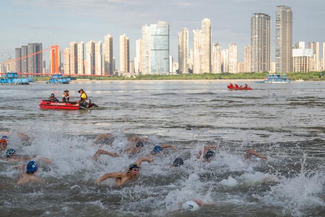 (260717) -- WUHAN, July 17, 2026 (Xinhua) -- Participants compete during the 51st edition of the Yangtze River crossing event in Wuhan, central China's Hubei Province, July 16, 2026. Located at the confluence of the Yangtze River and its longest tributary, the Han River, Wuhan is home to 165 rivers and 166 lakes. These abundant water resources foster a deep-seated love for open-water swimming among Wuhan's inhabitants.
   This year marks the 51st edition of the Yangtze River crossing event. During the competition, swimmers from around the country and the world gather on the banks of the Yangtze River to race across the river. Yet behind every crossing, members of a volunteer team, the Yangtze River volunteer lifeguard team, always safeguard participants' safety with passion, courage and selfless dedication.
   Zhou Zhuan, 64, is a detachment captain of the Yangtze River volunteer lifeguard Team. This year marks his fourth time participating in rescue support work during the river crossing event. As a native of Wuhan who grew up by the river, Zhou has a deep affection for the Yangtze River. Having loved swimming for many years and wishing to contribute to the community, Zhou joined the team after retiring from work in 2017.
   On regular days, Zhou and team members conduct swimming training and riverbank patrols, carry out simulated rescues, and deliver safety awareness outreach program. During the summer flood season, members of the team take turns on duty along the riverbank to respond to emergencies. Established in 2010, the team now comprises over 3,500 members and has rescued more than 1,200 people to date. (Xinhua/Du Zixuan)