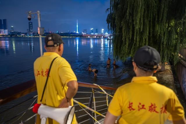 (260717) -- WUHAN, July 17, 2026 (Xinhua) -- Members of Yangtze River volunteer lifeguard team stand guard at a park in Wuhan, central China's Hubei Province, July 10, 2026. Located at the confluence of the Yangtze River and its longest tributary, the Han River, Wuhan is home to 165 rivers and 166 lakes. These abundant water resources foster a deep-seated love for open-water swimming among Wuhan's inhabitants.
   This year marks the 51st edition of the Yangtze River crossing event. During the competition, swimmers from around the country and the world gather on the banks of the Yangtze River to race across the river. Yet behind every crossing, members of a volunteer team, the Yangtze River volunteer lifeguard team, always safeguard participants' safety with passion, courage and selfless dedication.
   Zhou Zhuan, 64, is a detachment captain of the Yangtze River volunteer lifeguard Team. This year marks his fourth time participating in rescue support work during the river crossing event. As a native of Wuhan who grew up by the river, Zhou has a deep affection for the Yangtze River. Having loved swimming for many years and wishing to contribute to the community, Zhou joined the team after retiring from work in 2017.
   On regular days, Zhou and team members conduct swimming training and riverbank patrols, carry out simulated rescues, and deliver safety awareness outreach program. During the summer flood season, members of the team take turns on duty along the riverbank to respond to emergencies. Established in 2010, the team now comprises over 3,500 members and has rescued more than 1,200 people to date. (Xinhua/Du Zixuan)