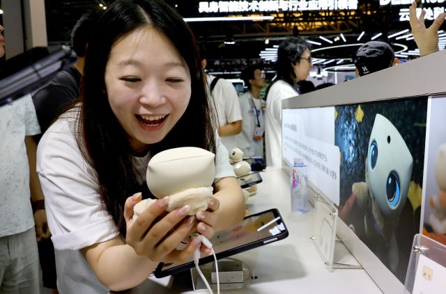 (260718) -- SHANGHAI, July 18, 2026 (Xinhua) -- A visitor interacts with a small robot during the 2026 World AI Conference and High-Level Meeting on Global AI Governance in Shanghai, east China, July 18, 2026. The event scheduled from Friday to Monday showcases exhibitions of smart devices, AI plus culture and entertainment experiences, and a wide range of cutting-edge AI products, among which a range of humanoid robots and AI-powered dexterous hands as one of the highlights. 
During the event, a variety of intelligent robots adaptable to diverse scenarios for industrial production and daily life are displayed. Notably, the country's annual output of humanoid robots is projected to exceed 100,000 units this year. (Xinhua/Fang Zhe)