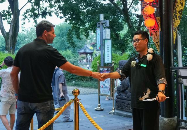 (260718) -- CHENGDU, July 18, 2026 (Xinhua) -- Yuan Xilin (R) shakes hands with a tourist from Spain after a Sichuan opera performance in Chengdu, southwest China's Sichuan Province, July 8, 2026. At 34, Yuan Xilin works as a ticket attendant at a Sichuan Opera theater in Chengdu, where he checks tickets, welcomes visitors and helps audiences find their way into the theater.
As Chengdu attracts growing numbers of international visitors interested in traditional Chinese opera and Sichuan Opera, Yuan meets dozens of overseas tourists every day. Hoping to make them feel more at ease, he began learning simple greetings in different languages so he could welcome them in their native tongue.
Yuan's interest in languages began in high school, when he came across a booklet introducing several foreign languages. Drawn to the rhythm of Spanish music and the sound of classical guitar, he developed a particular interest in Spanish.
As China's visa-free transit and other travel facilitation policies have brought more international visitors to the country, Yuan has expanded his language skills from English and Spanish to Italian, French, Portuguese, Russian, Polish and more. What once began with a simple greeting has gradually grown into brief conversations about visitors' experiences in China and introductions to Chengdu's local culture.
For Yuan, language is a bridge between cultures. He believes that even a simple greeting in a visitor's native language can make them feel welcome while creating opportunities for cultural exchange and his own personal growth. (Xinhua/Wang Xi)