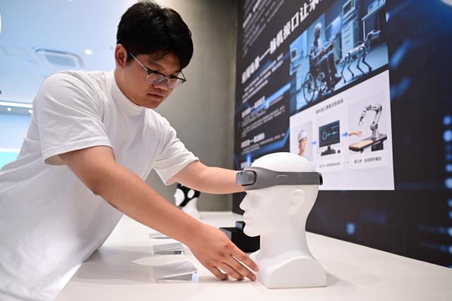 (260718) -- BENGBU, July 18, 2026 (Xinhua) -- A staff member demonstrates a brain health monitoring headband at the exhibition hall of China Sensor Valley in Bengbu, east China's Anhui Province, July 17, 2026. Bengbu, a traditional industrial city, has stepped up the development of its brain-computer interface (BCI) industry in recent years. By strengthening collaboration among industry, research institutes and medical institutions, Bengbu has built an innovation ecosystem that supports both BCI research and clinical application, aiming to become an emerging BCI innovation hub in the Yangtze River Delta region. (Xinhua/Zhou Mu)