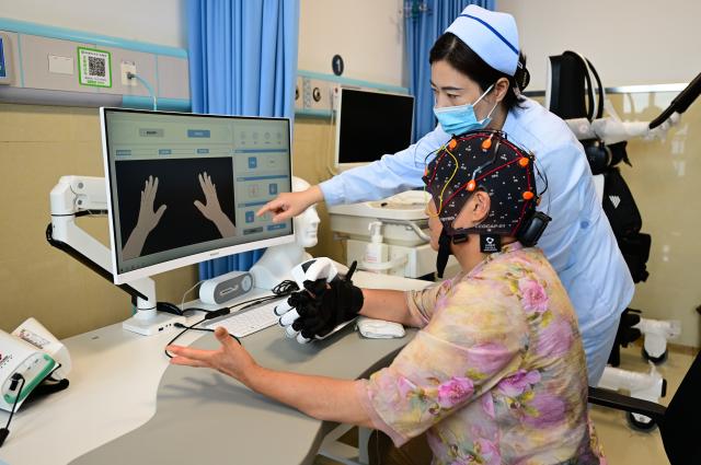 (260718) -- BENGBU, July 18, 2026 (Xinhua) -- A medical worker guides a patient to use a brain-computer interface (BCI) device for hand rehabilitation at a hospital in Bengbu, east China's Anhui Province, July 17, 2026. Bengbu, a traditional industrial city, has stepped up the development of its brain-computer interface (BCI) industry in recent years. By strengthening collaboration among industry, research institutes and medical institutions, Bengbu has built an innovation ecosystem that supports both BCI research and clinical application, aiming to become an emerging BCI innovation hub in the Yangtze River Delta region. (Xinhua/Zhou Mu)