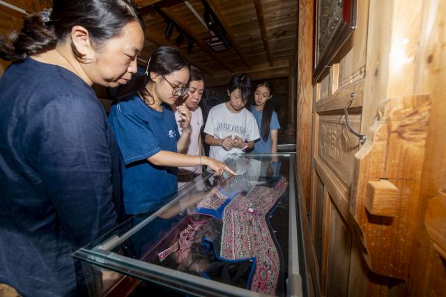 (260718) -- QIANDONGNAN, July 18, 2026 (Xinhua) -- A teacher (2nd L) introduces traditional clothes of the Dong people to children and parents from Shanghai in Meide Village of Congjiang County, Qiandongnan Miao and Dong Autonomous Prefecture, southwest China's Guizhou Province, July 18, 2026. In the summer vacation, a surging number of students from big cities like Shanghai and Shenzhen come to Meide Village of Qiandongnan Miao and Dong Autonomous Prefecture for a study tour, living with local people and experiencing the culture and customs of the Dong ethnic group. (Photo by Wu Dejun/Xinhua)