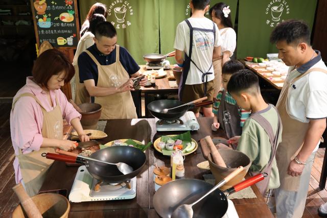 (260719) -- KUNMING, July 19, 2026 (Xinhua) -- Tourists learn to cook specialty dishes of the Dai ethnic group in Jinghong City, southwest China's Yunnan Province, July 19, 2026. (Photo by Li Yunsheng/Xinhua)