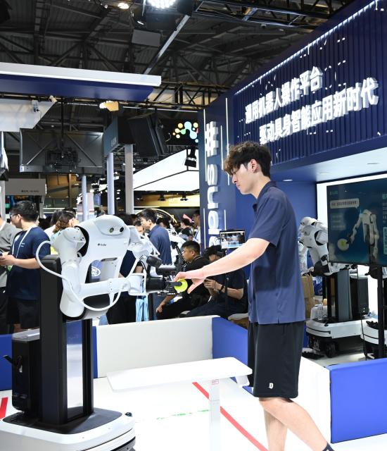 (260719) -- SHANGHAI, July 19, 2026 (Xinhua) -- A robot takes over an object from a staff member during the 2026 World AI Conference in Shanghai, east China, July 19, 2026. The ongoing 2026 World AI Conference turns out to be a highly competitive arena for general embodied AI products from more than 200 providers. It refers to a general-purpose intelligence system that enables robots to perform variable tasks and adapt to different application scenarios. (Xinhua/Huang Xiaoyong)