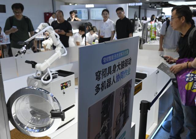 (260719) -- SHANGHAI, July 19, 2026 (Xinhua) -- A robot opens the door of a washing machine to load clothes for laundering during the 2026 World AI Conference in Shanghai, east China, July 19, 2026. The ongoing 2026 World AI Conference turns out to be a highly competitive arena for general embodied AI products from more than 200 providers. It refers to a general-purpose intelligence system that enables robots to perform variable tasks and adapt to different application scenarios. (Xinhua/Huang Xiaoyong)