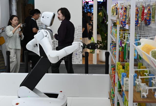 (260719) -- SHANGHAI, July 19, 2026 (Xinhua) -- A robot fetches a bottled beverage from a shelf during the 2026 World AI Conference in Shanghai, east China, July 19, 2026. The ongoing 2026 World AI Conference turns out to be a highly competitive arena for general embodied AI products from more than 200 providers. It refers to a general-purpose intelligence system that enables robots to perform variable tasks and adapt to different application scenarios. (Xinhua/Huang Xiaoyong)