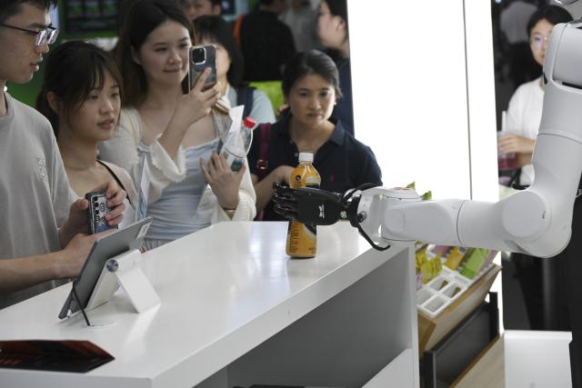 (260719) -- SHANGHAI, July 19, 2026 (Xinhua) -- A robot hands beverage to visitors during the 2026 World AI Conference in Shanghai, east China, July 19, 2026. The ongoing 2026 World AI Conference turns out to be a highly competitive arena for general embodied AI products from more than 200 providers. It refers to a general-purpose intelligence system that enables robots to perform variable tasks and adapt to different application scenarios. (Xinhua/Huang Xiaoyong)