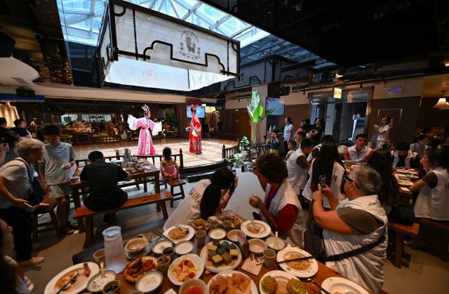 (260720) -- HAIKOU, July 20, 2026 (Xinhua) -- Tourists enjoy Laobacha dishes and Qiong Opera performance at a teahouse in Haikou, south China's Hainan Province, July 19, 2026. Hainan is seeing a surge in visitors during the summer holiday season. (Xinhua/Guo Cheng)