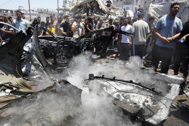 (260720) -- GAZA, July 20, 2026 (Xinhua) -- Palestinians stand around a burned vehicle following an Israeli drone strike in Gaza City, on July 20, 2026. A drone struck a civilian vehicle in central Gaza City, injuring 14 people, including women and children, a source with the ambulance and emergency services told Xinhua. Four Palestinians were killed on Monday in two Israeli drone strikes targeting vehicles in the Gaza Strip, according to Palestinian security and medical sources. (Photo by Rizek Abdeljawad/Xinhua)