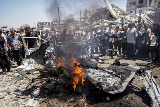 (260720) -- GAZA, July 20, 2026 (Xinhua) -- Palestinians stand around a burned vehicle following an Israeli drone strike in Gaza City, on July 20, 2026. A drone struck a civilian vehicle in central Gaza City, injuring 14 people, including women and children, a source with the ambulance and emergency services told Xinhua. Four Palestinians were killed on Monday in two Israeli drone strikes targeting vehicles in the Gaza Strip, according to Palestinian security and medical sources. (Photo by Rizek Abdeljawad/Xinhua)