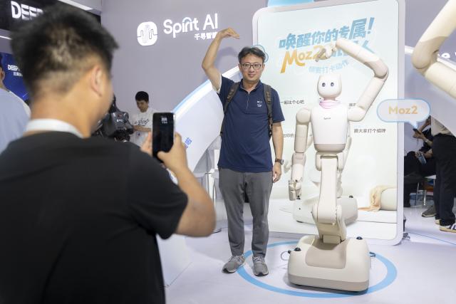 (260721) -- BEIJING, July 21, 2026 (Xinhua) -- A visitor and a humanoid robot make heart gestures as they pose for photos during the 2026 World AI Conference and High-Level Meeting on Global AI Governance in Shanghai, east China, July 20, 2026. The 2026 World AI Conference and High-Level Meeting on Global AI Governance concluded here on Monday. (Xinhua/Wang Xiang)