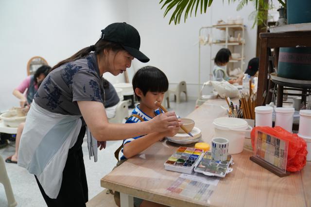 (260721) -- JINGDEZHEN, July 21, 2026 (Xinhua) -- A child engages in a hands-on porcelain-painting experience in Jingdezhen, east China's Jiangxi Province, July 1, 2026. Featuring various museums, hands-on porcelain-making experiences, diverse ceramic art installations, and a slow-paced lifestyle, Jingdezhen has become a trendy destination for young tourists during the summer vacation. (Xinhua/Zhou Mi)
