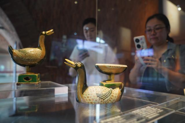 (260721) -- JINGDEZHEN, July 21, 2026 (Xinhua) -- A visitor takes photos of duck-shaped ceramic incense burners at the Jingdezhen Imperial Kiln Institute in Jingdezhen, east China's Jiangxi Province, May 26, 2026. Featuring various museums, hands-on porcelain-making experiences, diverse ceramic art installations, and a slow-paced lifestyle, Jingdezhen has become a trendy destination for young tourists during the summer vacation. (Xinhua/Wan Xiang)