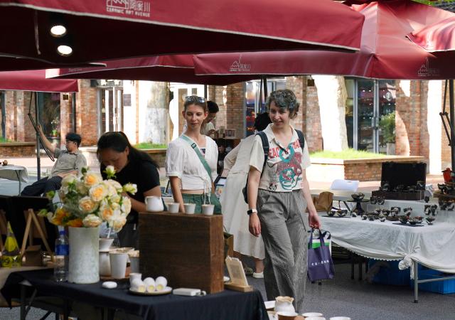 (260721) -- JINGDEZHEN, July 21, 2026 (Xinhua) -- Foreign tourists visit the Taoxichuan Ceramic Art Avenue in Jingdezhen, east China's Jiangxi Province, July 15, 2026. Featuring various museums, hands-on porcelain-making experiences, diverse ceramic art installations, and a slow-paced lifestyle, Jingdezhen has become a trendy destination for young tourists during the summer vacation. (Xinhua/Wan Xiang)