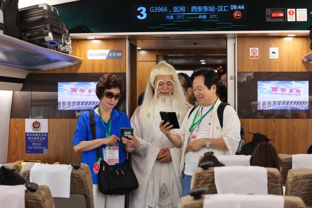 (260723) -- BEIJING, July 23, 2026 (Xinhua) -- South Korean tourists interact with a performer in a carriage of the bullet train No. G3966, the first high-speed train of Xi'an-Shiyan high-speed railway running from Xi'an East Railway Station to Hankou Railway Station, on June 30, 2026. (Photo by Liu Xiang/Xinhua)