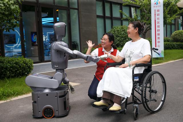 (260723) -- JINAN, July 23, 2026 (Xinhua) -- A staff member of domestic services and a senior citizen interact with a nursing robot in Jinan City, east China's Shandong Province, July 22, 2026. A number of domestic services brands have emerged in Shandong in recent years, offering widely ranging services such as eldercare, maternity care, and in-home caregiving. (Photo by Hao Xincheng/Xinhua)