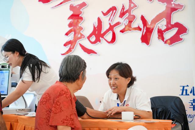 (260723) -- JINAN, July 23, 2026 (Xinhua) -- A staff member of domestic services measures blood pressure for a senior citizen in Heze City, east China's Shandong Province, July 20, 2026. A number of domestic services brands have emerged in Shandong in recent years, offering widely ranging services such as eldercare, maternity care, and in-home caregiving. (Photo by Li Baozhu/Xinhua)
