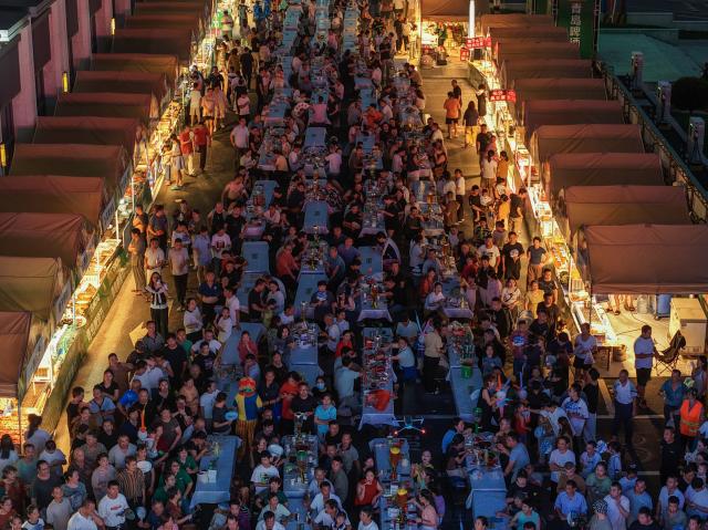 (260725) -- JIANDE, July 25, 2026 (Xinhua) -- An aerial drone photo taken on July 24, 2026 shows people enjoying foods and drinks at a beer festival in Jiande City of east China's Zhejiang Province. A summer beer festival kicked off at a farmers market here on Friday. Featuring live performances, gourmet foods and drinks, leisure activities and bazaars, the event attracted thousands of locals and tourists. (Xinhua/Xu Yu)