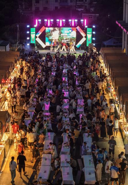 (260725) -- JIANDE, July 25, 2026 (Xinhua) -- An aerial drone photo taken on July 24, 2026 shows people enjoying foods and drinks and watching a performance at a beer festival in Jiande City of east China's Zhejiang Province. A summer beer festival kicked off at a farmers market here on Friday. Featuring live performances, gourmet foods and drinks, leisure activities and bazaars, the event attracted thousands of locals and tourists. (Xinhua/Xu Yu)