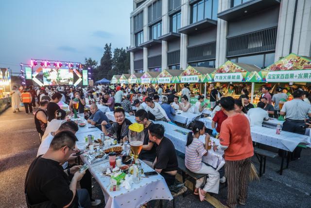 (260725) -- JIANDE, July 25, 2026 (Xinhua) -- People enjoy foods and drinks at a beer festival in Jiande City of east China's Zhejiang Province on July 24, 2026. A summer beer festival kicked off at a farmers market here on Friday. Featuring live performances, gourmet foods and drinks, leisure activities and bazaars, the event attracted thousands of locals and tourists. (Xinhua/Xu Yu)
